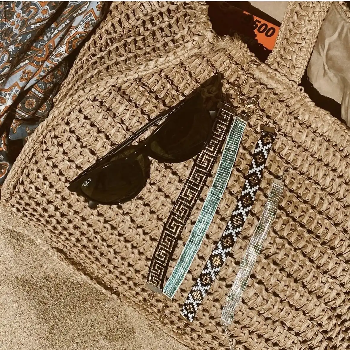 Pulseras miyuki tejidas sobre un canasto de playa junto a unos lentes de sol